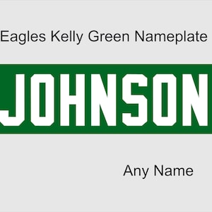 May include: A rectangular nameplate featuring a dark green horizontal bar with the white text JOHNSON in a bold, block-style font. Above the bar, the text Eagles Kelly Green Nameplate is printed, and below the bar, the text Any Name is visible.