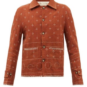 May include: Rust-colored jacket with white cross-stitch embroidery. The jacket features a classic collar, button-down front, and pockets with decorative stitching. The sleeves have buttoned cuffs, and the overall design is a blend of rustic and tailored elements.