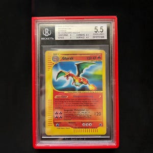 May include: A graded Pok&eacute;mon card featuring a Charizard, labeled "Glurak" in German. The card is encased in a red holder with a Beckett grading of 5.5. The card's design includes a fiery dragon illustration.