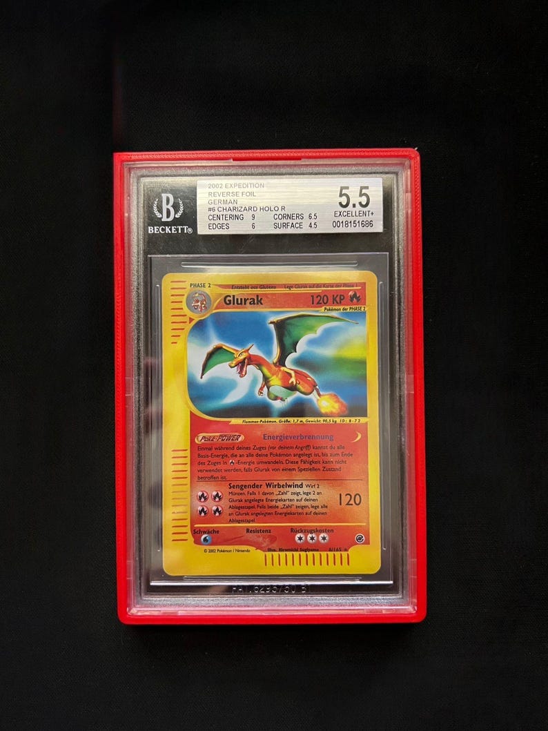 May include: A graded Pok&eacute;mon card featuring a Charizard, labeled "Glurak" in German. The card is encased in a red holder with a Beckett grading of 5.5. The card's design includes a fiery dragon illustration.