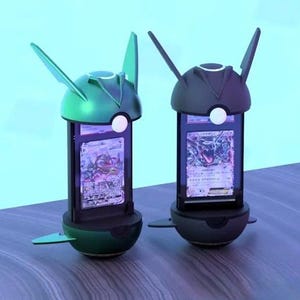 K&ouml;nnte beinhalten: Zwei futuristische Kartenst&auml;nder, einer gr&uuml;n und einer dunkelgrau, halten jeweils eine Sammelkarte. Die St&auml;nder haben einen abgerundeten Sockel, eine rechteckige Anzeigefl&auml;che und eine stilisierte Oberseite mit fl&uuml;gelartigen Elementen. Die Karten sind sichtbar.