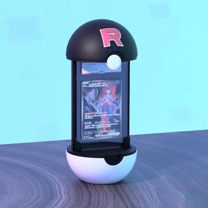 K&ouml;nnte beinhalten: Eine schwarz-wei&szlig;e Vitrine in Form eines Pok&eacute; Balls mit einem schwarzen Oberteil mit einem roten "R"-Logo. Die Vitrine enth&auml;lt eine Sammelkarte mit einer farbenfrohen Illustration. Der Sockel ist wei&szlig; und das Oberteil ist schwarz.