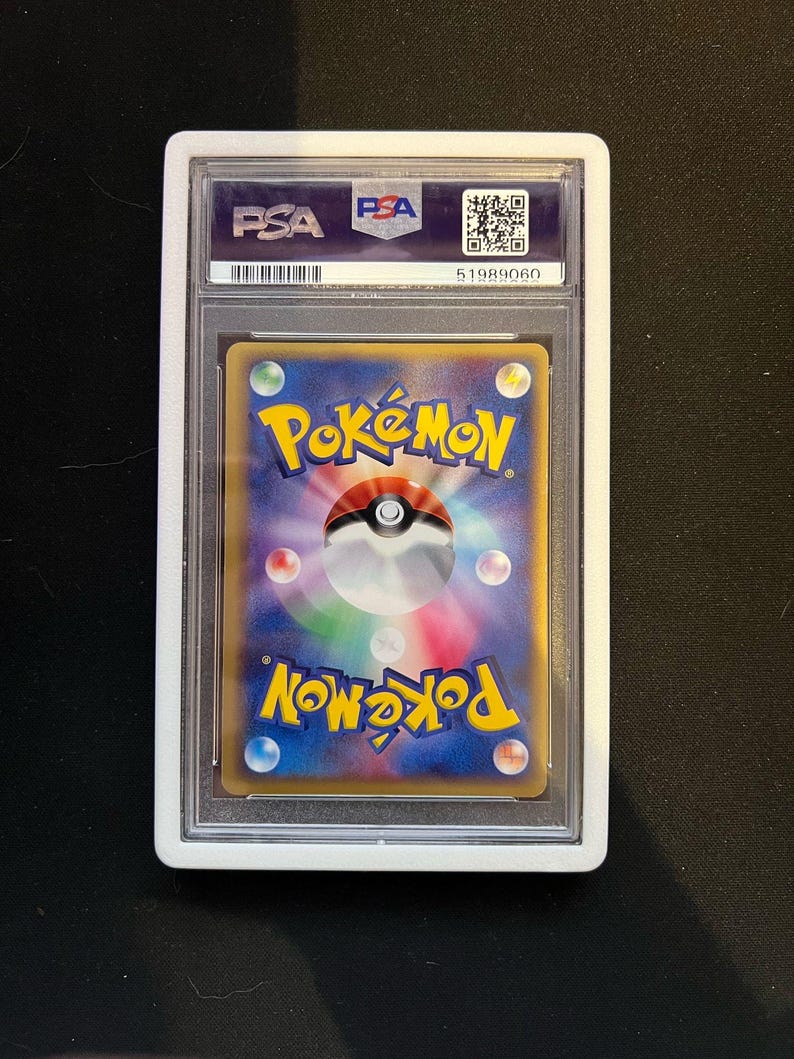 May include: A graded Pok&eacute;mon trading card in a clear plastic case. The card shows the Pok&eacute;mon logo and a Pok&eacute; Ball. The holder has a white border and the PSA logo.