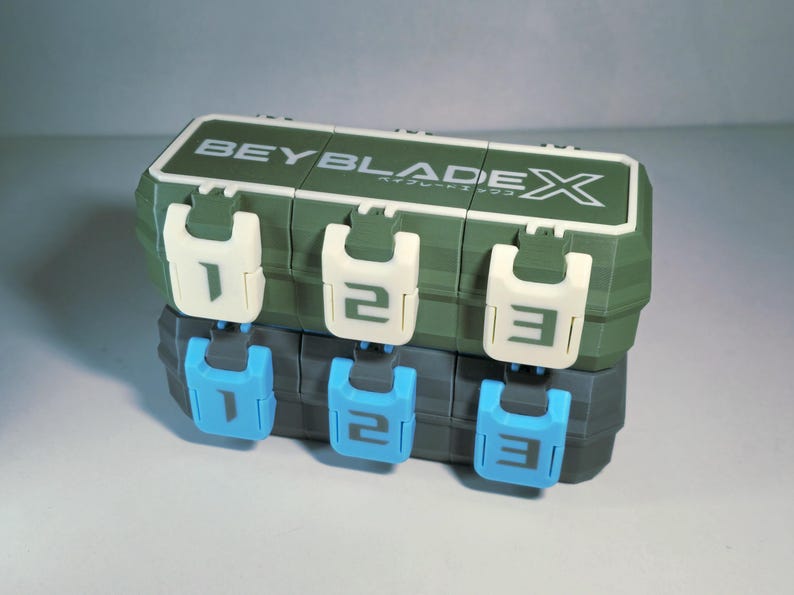 May include: A green and white plastic storage container with the text "BEYBLADE X" on top. The container has three white latches with the numbers 1, 2, and 3. Below are three blue latches with the same numbers.
