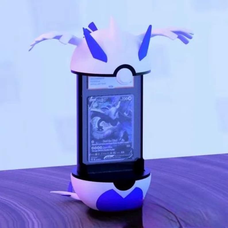 K&ouml;nnte beinhalten: Ein wei&szlig;-blauer Pok&eacute;mon-Karten-Pr&auml;sentationsst&auml;nder. Der St&auml;nder hat ein stilisiertes Design mit fl&uuml;gelartigen Elementen und einem zentralen Anzeigebereich, der eine Karte h&auml;lt. Die Karte zeigt eine blau-wei&szlig;e Illustration einer drachenartigen Kreatur.