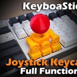 Könnte beinhalten: Eine Tastatur mit einem individuellen Joystick-Keycap. Das Keycap ist gelb und hat eine rote Kugel oben. Der Text "KeyboaStick" und "Joystick Keycap Full Functional" sind zu sehen.