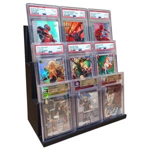 May include: A black tiered display stand holding multiple graded trading cards. The cards feature colorful illustrations of comic book and anime characters. The cards are encased in clear protective holders.