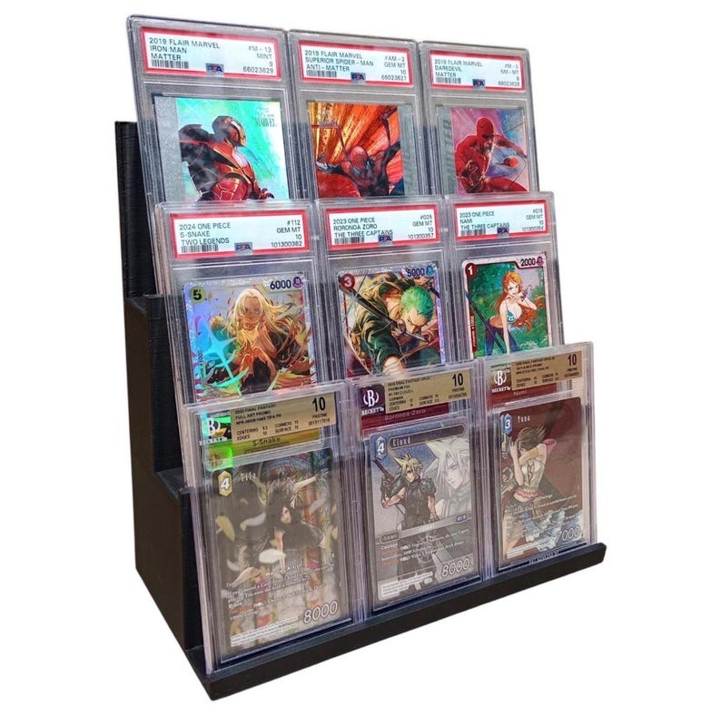 May include: A black tiered display stand holding multiple graded trading cards. The cards feature colorful illustrations of comic book and anime characters. The cards are encased in clear protective holders.