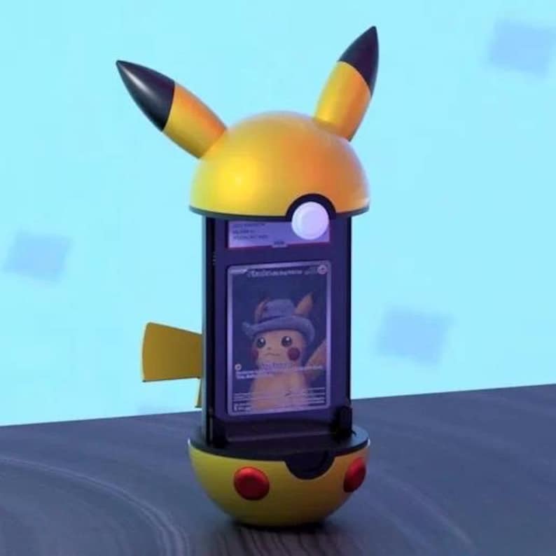 K&ouml;nnte beinhalten: Ein gelb-schwarzes Pikachu-Display mit einer Karte, die ein Pikachu mit Hut zeigt. Das Display hat einen abgerundeten Sockel mit roten Akzenten und hohe, spitze Ohren. Die Karte ist durch ein klares Fenster sichtbar.