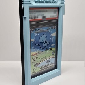 Op de afbeelding: Een lichtblauw 3D-geprint frame dat lijkt op een Nintendo Game Boy, met een Pok&eacute;mon-verzamelkaart. De kaart toont een blauw wezen en Japanse tekst. Het frame heeft de tekst "Nintendo GAME BOY" in reli&euml;f.