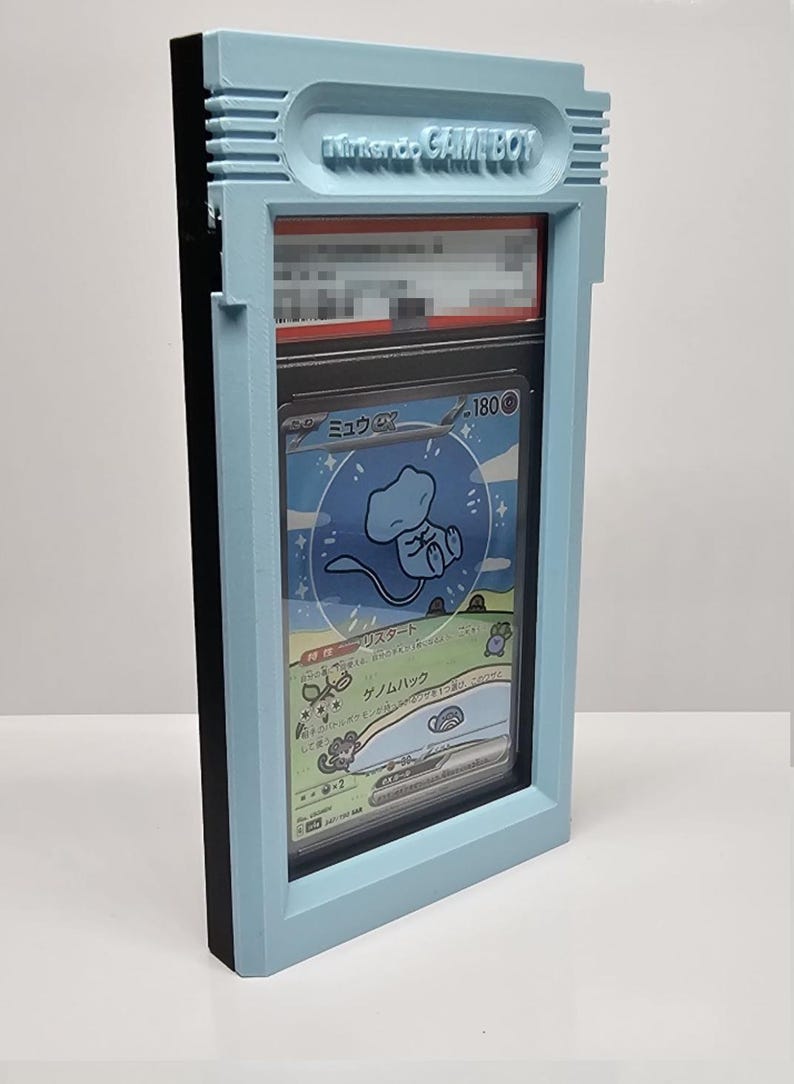 Op de afbeelding: Een lichtblauw 3D-geprint frame dat lijkt op een Nintendo Game Boy, met een Pok&eacute;mon-verzamelkaart. De kaart toont een blauw wezen en Japanse tekst. Het frame heeft de tekst "Nintendo GAME BOY" in reli&euml;f.