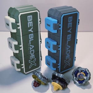 May include: Two toy storage cases and three spinning tops. The cases are green and gray with the text "BEYBLADE X" and Japanese text. The spinning tops are various colors, including yellow, purple, and blue.