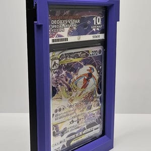 Op de afbeelding: Een paarse Game Boy-vormige displaycase met een beoordeelde Pok&eacute;mon-kaart. De kaart is een Deoxys VSTAR Special Art Rare, beoordeeld met een 10 door GEM MINT. De case heeft de tekst "Nintendo GAME BOY" bovenaan.