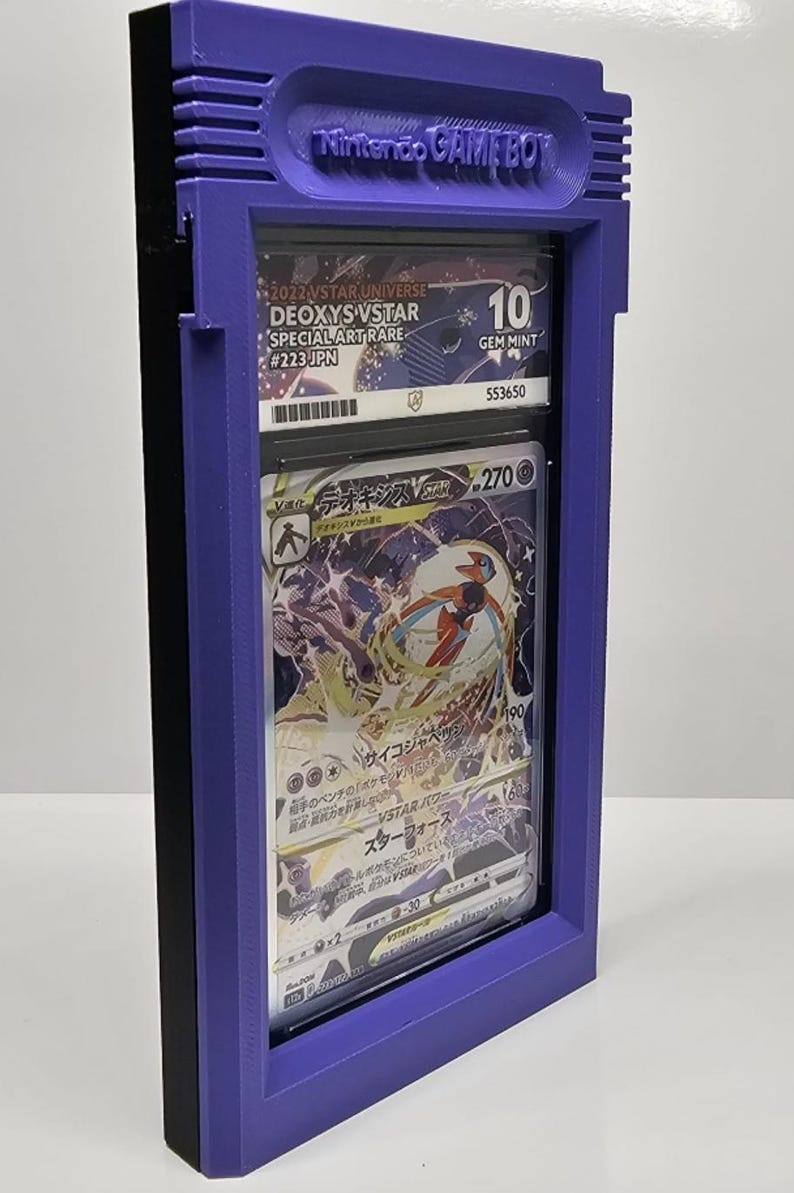 Op de afbeelding: Een paarse Game Boy-vormige displaycase met een beoordeelde Pok&eacute;mon-kaart. De kaart is een Deoxys VSTAR Special Art Rare, beoordeeld met een 10 door GEM MINT. De case heeft de tekst "Nintendo GAME BOY" bovenaan.