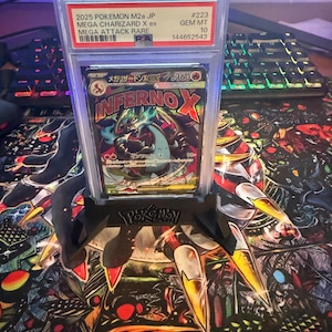 Può includere: Una carta Pokémon valutata con Mega Charizard X ex, etichettata come Mega Attack Rare. La carta è racchiusa in un supporto protettivo con un grado GEM MT 10. L'artwork della carta mostra un Charizard infuocato con il testo "INFERNO X".
