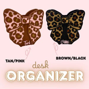 May include: Two bow-shaped desk organizers with leopard print patterns. The left organizer is tan and pink with the name Tori, and the right organizer is brown and black with the name Vikki. Text reads: TAN/PINK, BROWN/BLACK, desk, ORGANIZER.