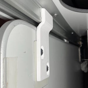 Könnte beinhalten: Nahaufnahme eines weißen Kunststoff-Türverschlusses und Schienensystems. Der Verschluss ist an einer weißen Tür montiert und mit schwarzen Schrauben befestigt. Die Schiene ist silberfarben und verläuft entlang der Oberseite des Türrahmens.