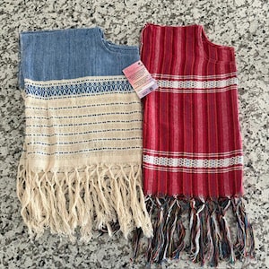 Puede incluir: Dos textiles tejidos rectangulares con bordes de flecos. Uno presenta una sección superior azul y una sección inferior crema con rayas horizontales azules. El otro es rojo con rayas verticales en tonos de rojo y blanco. Incluye una etiqueta.