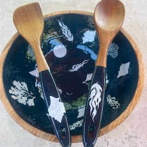 May include: A wooden salad bowl with a dark blue interior featuring white floral designs, accompanied by a wooden spoon and spatula. The handles of the utensils are dark blue with white decorative accents. The bowl has a natural wood rim.