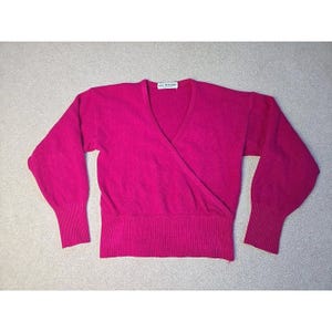 May include: A magenta wrap sweater with a V-neck and long sleeves. The sweater features ribbed cuffs and a ribbed hem. The label reads "Luce Pisanu".