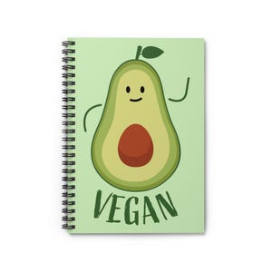 May include: A spiral-bound notebook with a light green cover featuring a cartoon avocado character. The avocado has a brown pit, a smiling face, and the word "VEGAN" in green letters below it. The notebook's pages are white.