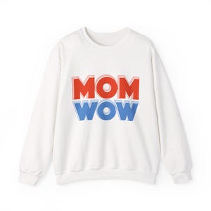 May include: A white sweatshirt featuring the text "MOM WOW" in red and blue block letters. The sweatshirt has a crew neck and long sleeves. The text is stacked, with "MOM" above "WOW".