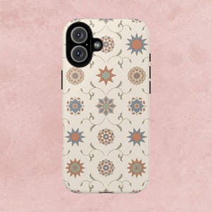 Peut inclure: Coque de téléphone avec un fond crème orné d'un motif répété d'étoiles et de motifs floraux dans des tons orange, bleu et beige. La coque a un module caméra noir et des boutons latéraux.