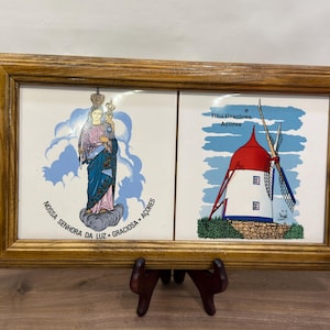 May include: A rectangular wooden serving tray with two side handles, featuring two inset ceramic tiles. The left tile depicts a figure in blue and pink robes with the text "NOSSA SENHORA DA LUZ - GRACIOSA - AÇORES". The right tile shows a windmill with the text "Ilha Graciosa Açores".