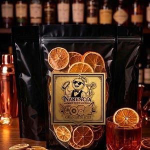 May include: A clear bag of dried orange slices with a gold label that reads "Narencia Premium Dried Garnishes Orange Slices". A cocktail glass with an orange slice garnish is on a wooden surface.