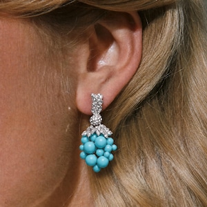 May include: A drop earring featuring a cluster of round, bright turquoise beads arranged in a grape-like shape. The top of the cluster is adorned with a silver-toned cap encrusted with small, clear, sparkling crystals, attached to a crystal-set post.