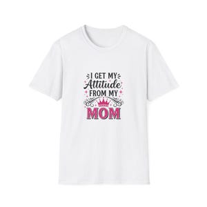 May include: White t-shirt with the text "I GET MY Attitude FROM MY MOM" in black and pink. The design includes a crown and star accents. A casual, everyday wear tee.