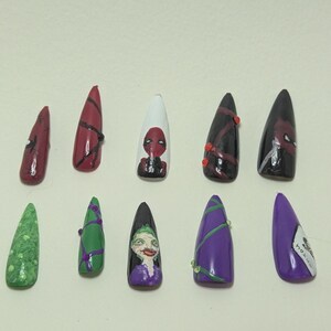 Peut inclure: Un ensemble de dix faux ongles en forme de stylet avec des motifs peints à la main. La rangée supérieure présente des motifs rouges et noirs avec un portrait de Deadpool. La rangée inférieure montre des designs verts et violets avec le Joker.