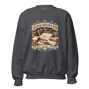 May include: A dark heather gray crewneck sweatshirt featuring a graphic of an archival research desk with books, a magnifying glass, and white gloves. The text reads ARCHIVAL RESEARCH DESK and PRESERVE • DESCRIBE • CONNECT in a decorative frame.