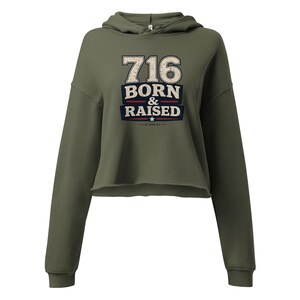 May include: An olive green cropped hoodie with long sleeves and a hood. The front features a distressed graphic with the text 716 BORN & RAISED in white and dark blue, accented by red horizontal lines and a small star, with 2020 KJ printed below.