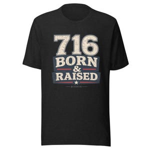 May include: A black short-sleeve t-shirt featuring a distressed graphic print in white, blue, and red. The text reads 716 BORN & RAISED with a small star below the text. The design has a weathered, vintage-inspired texture on the front center.
