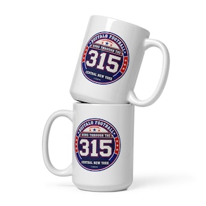 May include: Two white ceramic mugs stacked vertically, each featuring a circular blue and red graphic with the text Buffalo Football Runs Through The 315 Central New York, including a small football icon and stars, with a copyright date of 2020.