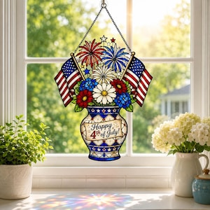 Könnte beinhalten: Ein Buntglas-Fensterhänger mit einer Vase, die den Text Happy 4th of July trägt, verziert mit roten, weißen und blauen Blumen, Feuerwerksmotiven und zwei amerikanischen Flaggen. Das Stück ist an einer schwarzen Metallkette am Fenster befestigt.