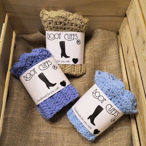 May include: Three pairs of crocheted boot cuffs in beige, blue, and light blue. Each pair has a label that says "BOOT CUFFS" and "Handmade for you, with love".