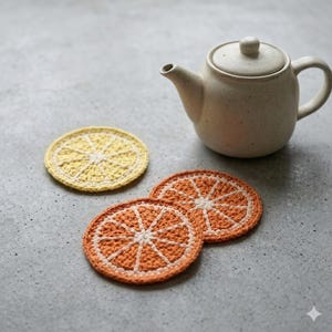 Peut inclure: Une théière en céramique crème avec un couvercle est posée à côté de trois dessous de verre crochetés. Deux dessous de verre sont orange et blancs, ressemblant à des tranches d'orange, et un est jaune et blanc, ressemblant à une tranche de citron.