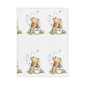 May include: White rectangular towel featuring a repeating pattern of Winnie the Pooh. Each illustration shows Pooh Bear in a red shirt, sitting next to a honey pot labeled "Hunny", with bees buzzing around him. The design is a whimsical, cartoon style.