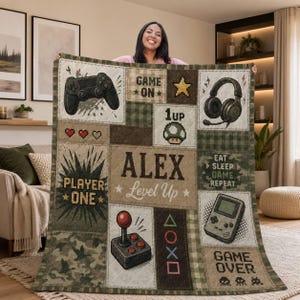 Op de afbeelding: Een doorgestikte deken met een gamingthema in camouflage- en ruitpatroon. Het toont een gamecontroller, koptelefoon, joystick, handheld console, pixelhartjes, een paddenstoel en de tekst: GAME ON, 1up, ALEX Level Up, PLAYER ONE, EAT SLEEP GAME REPEAT en GAME OVER.