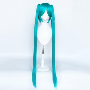 May include: A bright turquoise wig with long pigtails. The wig is displayed on a white mannequin head and stand, against a plain white background. The wig's colour is a bright, eye-catching shade of teal.