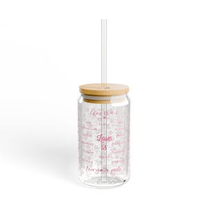 Puede incluir: Un vaso de vidrio transparente con tapa de bambú y pajita transparente. El vaso está decorado con un estampado floral rosa y las palabras "I Cor 13:4-7" y "Love is" en escritura rosa. También son visibles las palabras "Love never fails".