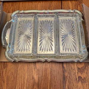 May include: A rectangular silver-toned serving tray featuring three distinct glass compartments. Each glass section displays a clear, pressed sunburst or starburst pattern. The tray has a scalloped, metallic rim with integrated handles.