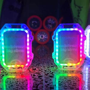 May include: Four clear, rectangular LED lights with the text "medjohnson big slime" are displayed. Each light has a colorful border of red, blue, green, and purple. The lights are reflected on a dark surface, with roller skate wheels in the background.