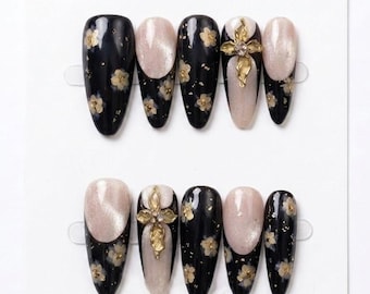 Uñas negras góticas hechas a mano con adornos florales dorados y puntas francesas estilo ojo de gato.