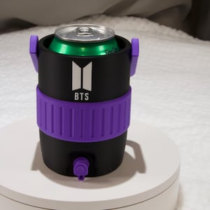 May include: A black cylindrical beverage can cooler featuring a purple ribbed band around the center and a small purple spout at the base. The front displays a white BTS logo with the text BTS underneath. A green soda can is inserted into the top.