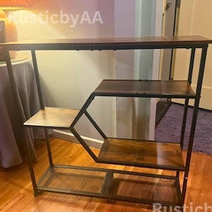May include: A multi-tiered, brown and black metal shelf unit. The unit has a rectangular top shelf, three additional shelves, and a wire mesh bottom shelf. The frame is black, and the shelves have a wood-grain finish.