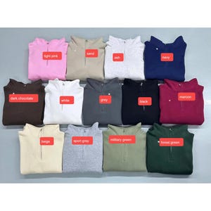 May include: A collection of twelve quarter-zip sweatshirts arranged in three rows, featuring colors labeled as light pink, sand, ash, navy, dark chocolate, white, grey, black, maroon, beige, sport grey, military green, and forest green.