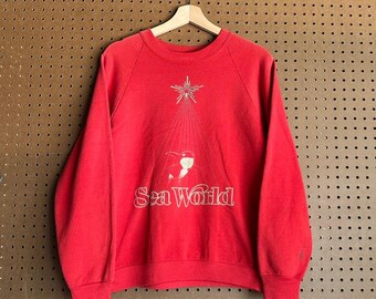 Vintage Sea World Weihnachts-Sweatshirt aus den 80er Jahren, verwaschenes rotes Raglan-Sweatshirt mit Rundhalsausschnitt und Shamu-Orca-Weihnachtsmotiv, passend für Damen in Größe S/M (Themenpark-Stil).